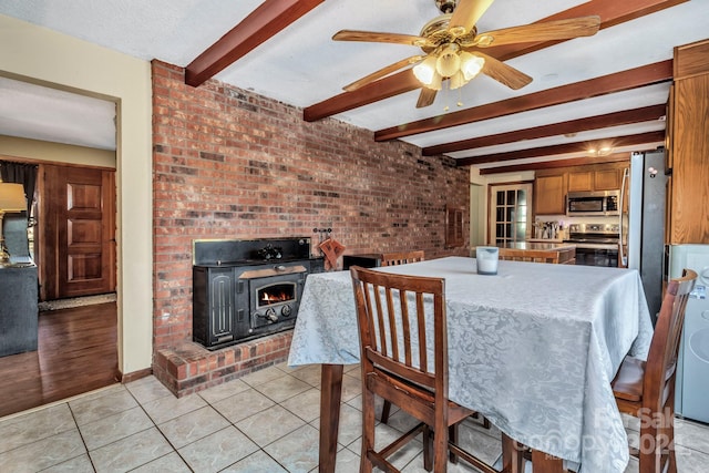 tiled dining room with beamed ceiling, ceiling fan, a fireplace, and brick wall