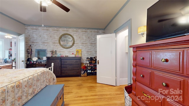 bedroom featuring ceiling fan, light hardwood / wood-style flooring, crown molding, and brick wall