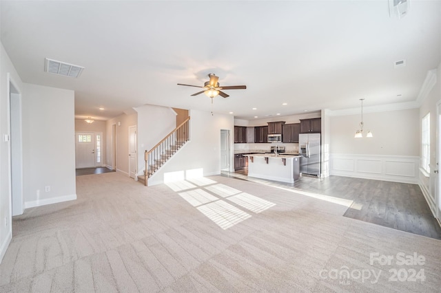 unfurnished living room with ceiling fan with notable chandelier, light colored carpet, and ornamental molding