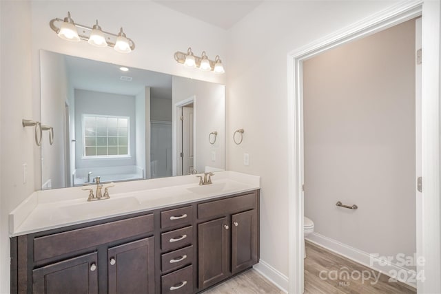 bathroom with a washtub, hardwood / wood-style floors, vanity, and toilet