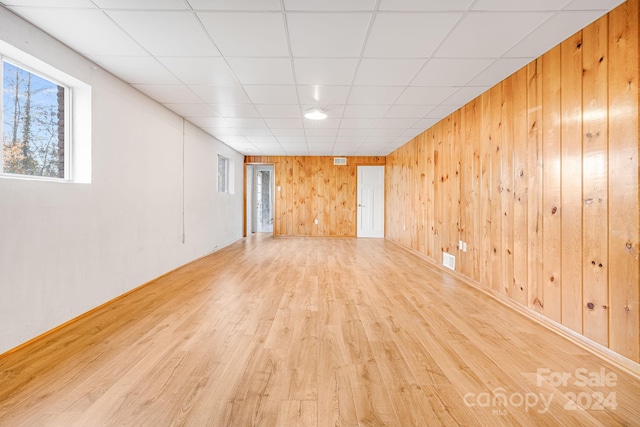 unfurnished room featuring a paneled ceiling, wood walls, and light hardwood / wood-style flooring