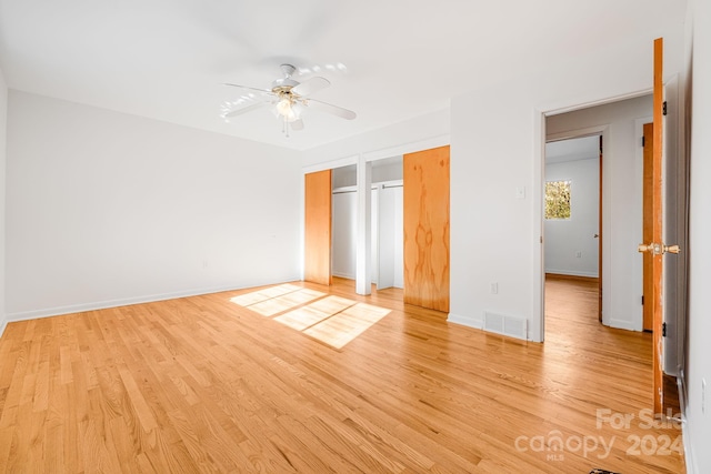 unfurnished bedroom with ceiling fan, two closets, and light hardwood / wood-style flooring