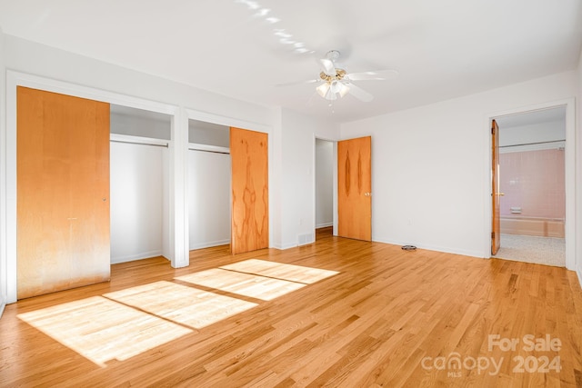 unfurnished bedroom featuring ceiling fan, light wood-type flooring, ensuite bathroom, and multiple closets