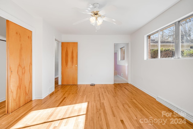 unfurnished bedroom featuring ceiling fan, a baseboard heating unit, ensuite bath, and light hardwood / wood-style flooring