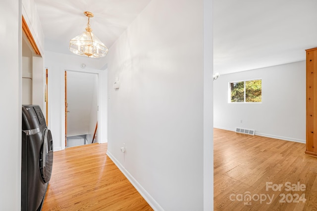 hall with separate washer and dryer, wood-type flooring, and an inviting chandelier