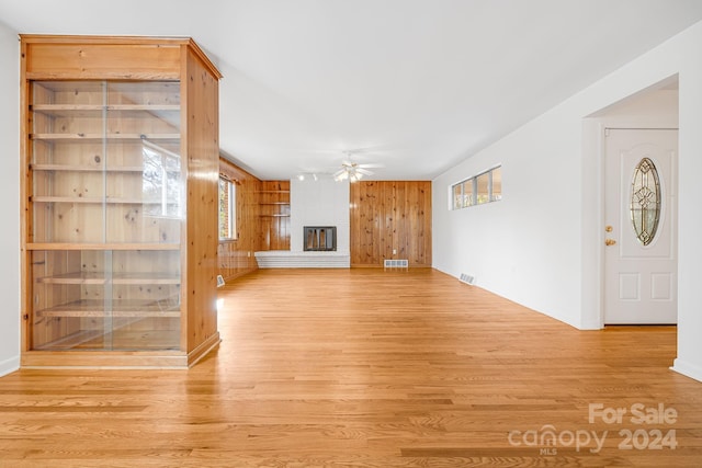 unfurnished living room with a fireplace, wooden walls, light hardwood / wood-style flooring, and ceiling fan