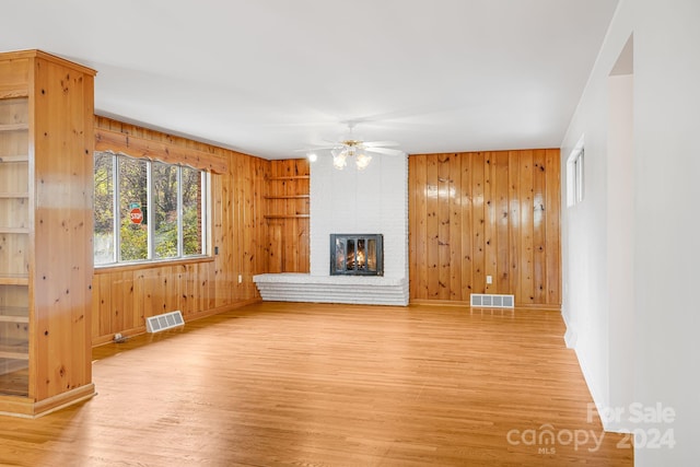 unfurnished living room featuring a fireplace, light wood-type flooring, ceiling fan, and wood walls