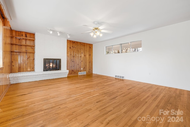 unfurnished living room with wood walls, light hardwood / wood-style flooring, ceiling fan, built in features, and a fireplace