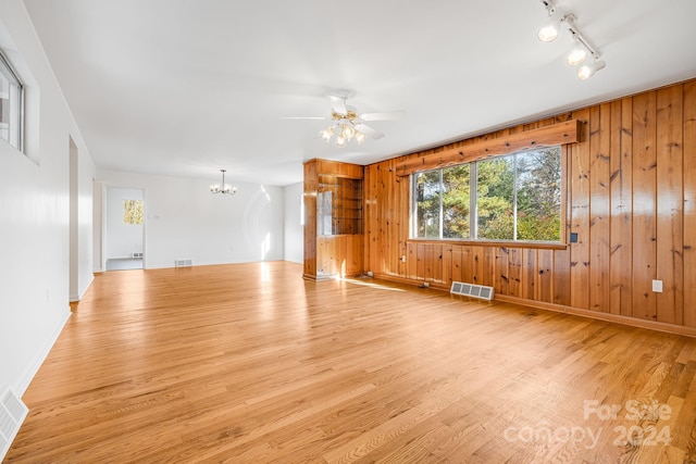 unfurnished living room with wood walls, ceiling fan with notable chandelier, and light wood-type flooring