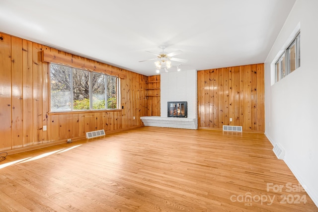 unfurnished living room with a fireplace, light hardwood / wood-style flooring, ceiling fan, and wood walls