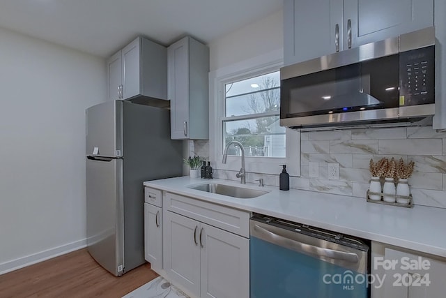 kitchen with tasteful backsplash, sink, stainless steel appliances, and light hardwood / wood-style floors