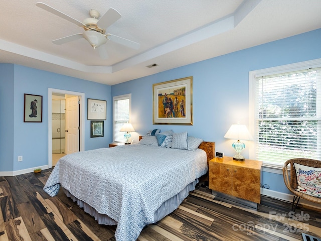 bedroom featuring multiple windows, dark wood-type flooring, a raised ceiling, and ceiling fan