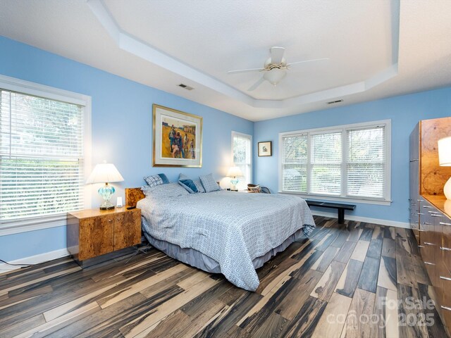 bedroom featuring ceiling fan, a tray ceiling, dark hardwood / wood-style flooring, and multiple windows