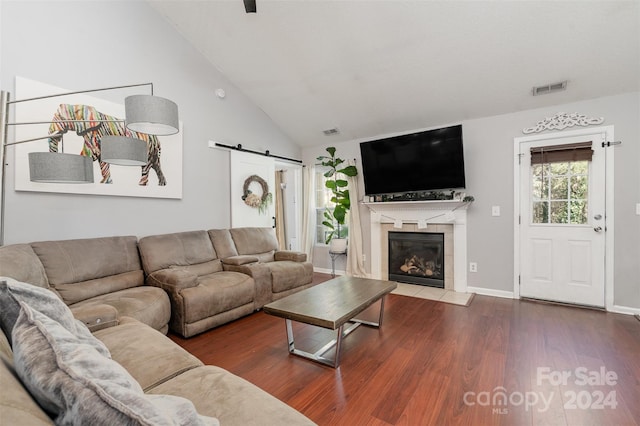 living room with a tiled fireplace, a barn door, wood-type flooring, and vaulted ceiling