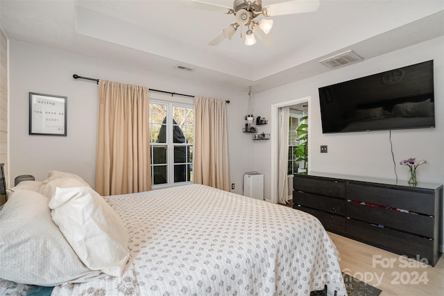 bedroom with a raised ceiling, ceiling fan, and light hardwood / wood-style flooring