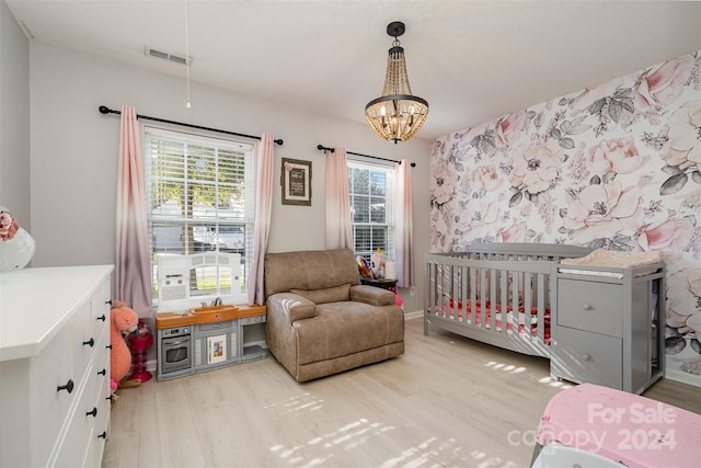 bedroom with light wood-type flooring, a crib, and an inviting chandelier