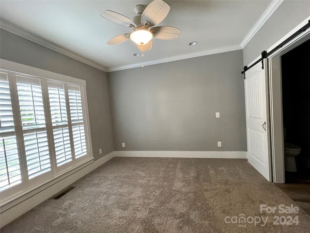 unfurnished bedroom with dark colored carpet, a barn door, ceiling fan, and crown molding