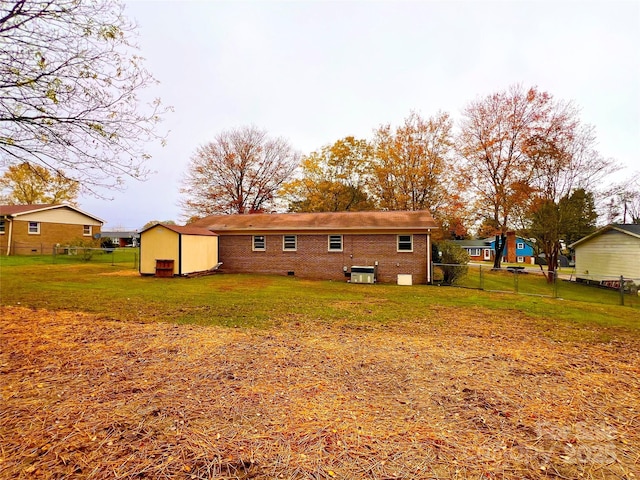 rear view of property featuring an outbuilding, a storage shed, brick siding, fence, and a lawn