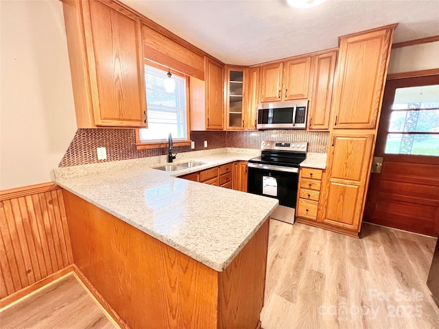 kitchen featuring appliances with stainless steel finishes, glass insert cabinets, a peninsula, light wood-type flooring, and a sink