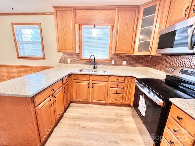 kitchen with light stone counters, a peninsula, stainless steel appliances, light wood-type flooring, and a sink