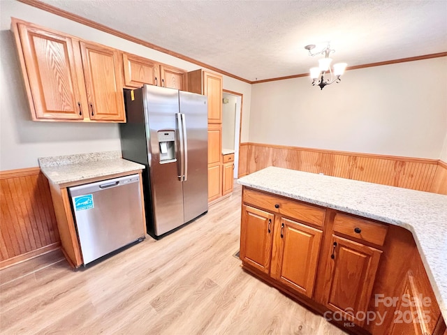 kitchen featuring light wood finished floors, appliances with stainless steel finishes, ornamental molding, wainscoting, and a textured ceiling