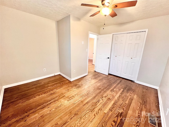 unfurnished bedroom featuring a textured ceiling, a closet, wood finished floors, and baseboards