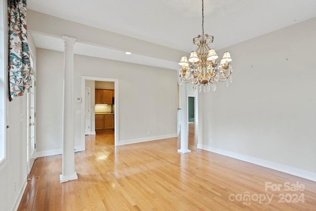 unfurnished room featuring light wood-type flooring, ornate columns, and a notable chandelier