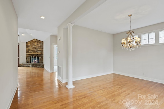 unfurnished room with a fireplace, vaulted ceiling, an inviting chandelier, and light hardwood / wood-style flooring