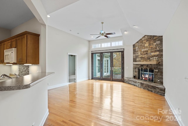 unfurnished living room with french doors, ceiling fan, high vaulted ceiling, light hardwood / wood-style flooring, and a stone fireplace