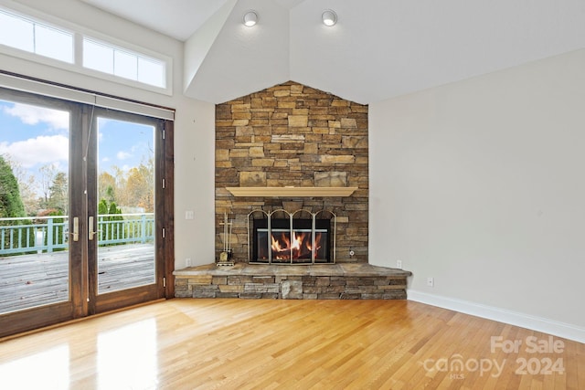 unfurnished living room featuring a stone fireplace, french doors, vaulted ceiling, and hardwood / wood-style flooring