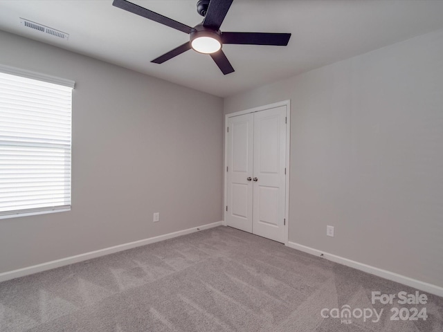 unfurnished bedroom with a closet, light colored carpet, and ceiling fan