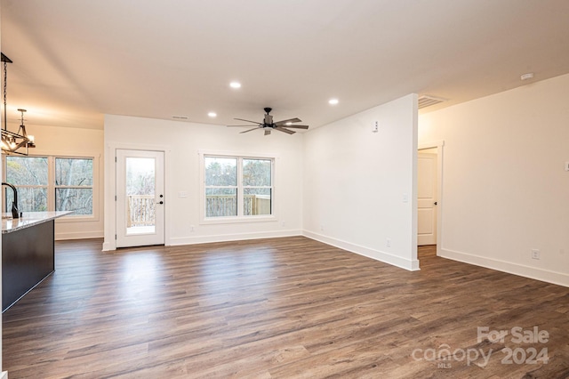 unfurnished living room featuring ceiling fan with notable chandelier and dark hardwood / wood-style floors