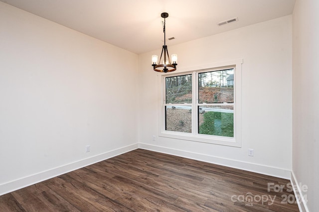 spare room with dark hardwood / wood-style floors and a notable chandelier