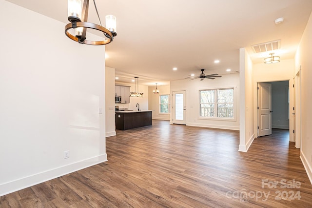 unfurnished living room with dark hardwood / wood-style floors, sink, and ceiling fan with notable chandelier