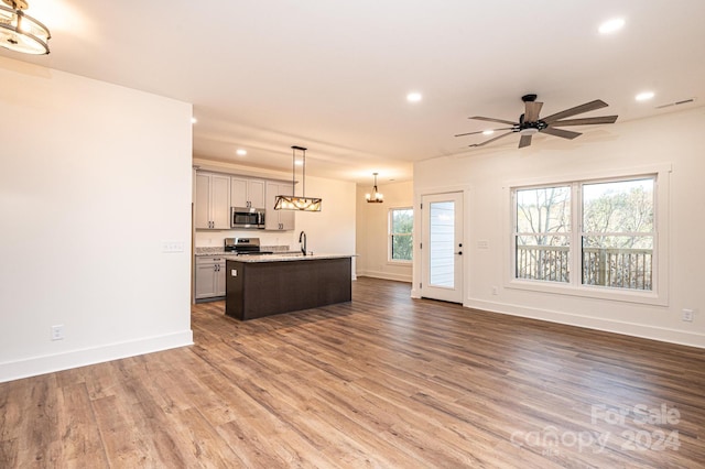 unfurnished living room with sink, ceiling fan with notable chandelier, and hardwood / wood-style flooring