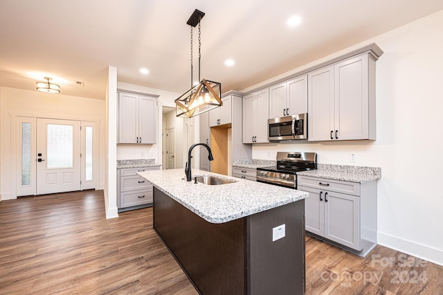 kitchen featuring sink, light stone counters, dark hardwood / wood-style flooring, a center island with sink, and appliances with stainless steel finishes