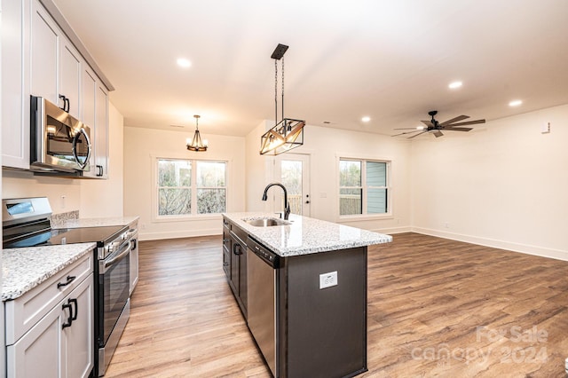 kitchen with appliances with stainless steel finishes, sink, light hardwood / wood-style flooring, hanging light fixtures, and an island with sink