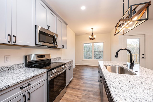 kitchen with light stone countertops, light wood-type flooring, stainless steel appliances, pendant lighting, and an inviting chandelier