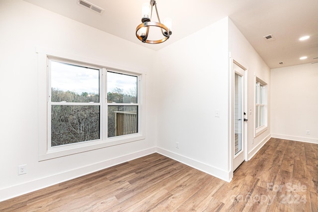 empty room with hardwood / wood-style flooring and an inviting chandelier