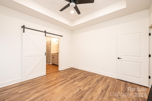 unfurnished bedroom featuring a barn door, ensuite bathroom, ceiling fan, and light hardwood / wood-style floors