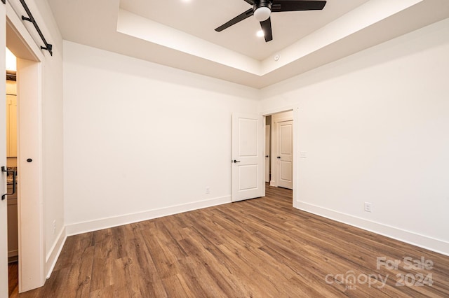 unfurnished room featuring a tray ceiling, a barn door, ceiling fan, and hardwood / wood-style flooring