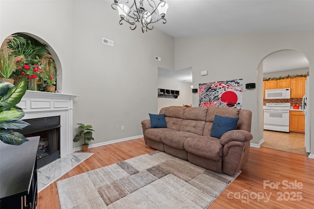 living room with arched walkways, a fireplace with flush hearth, visible vents, and light wood-style floors