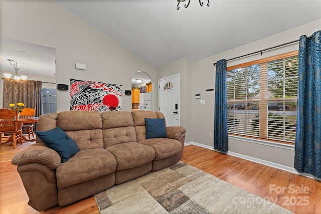 living area with light wood-type flooring, baseboards, arched walkways, and vaulted ceiling