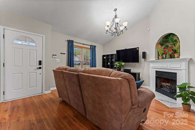 living area featuring baseboards, lofted ceiling, a fireplace with flush hearth, wood finished floors, and a chandelier