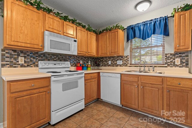 kitchen with a textured ceiling, light countertops, white appliances, and a sink