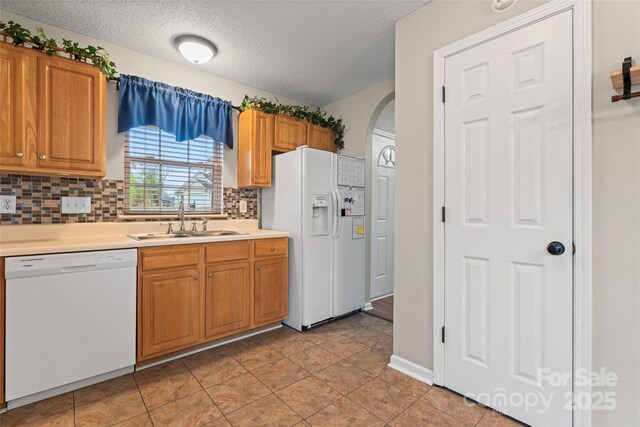 kitchen featuring arched walkways, a textured ceiling, white appliances, a sink, and light countertops