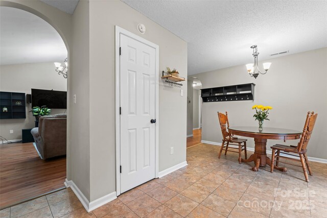 dining room featuring arched walkways, visible vents, an inviting chandelier, a textured ceiling, and baseboards