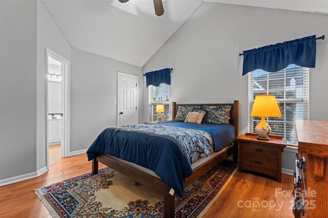 bedroom with ceiling fan, ensuite bath, wood finished floors, high vaulted ceiling, and baseboards