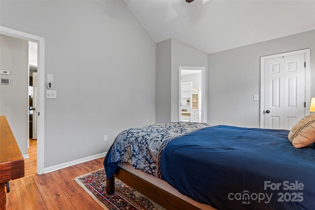 bedroom featuring lofted ceiling, connected bathroom, baseboards, and wood finished floors