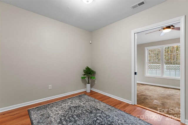 empty room with a ceiling fan, wood finished floors, visible vents, and baseboards